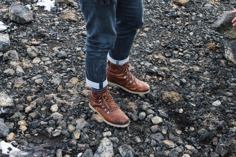 person wearing brown leather boots standing on rocky ground