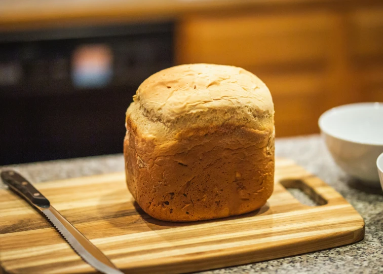 a loaf of bread sitting on top of a wooden  board next to a knife