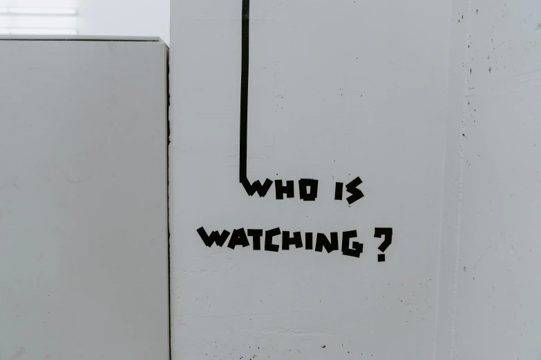 this bathroom stall has the words who is watching on it