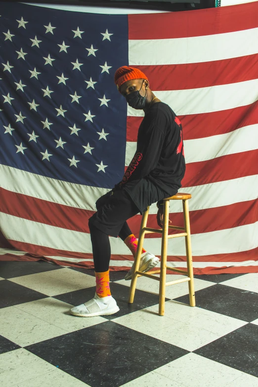 a person wearing an orange bandana, sitting on a stool