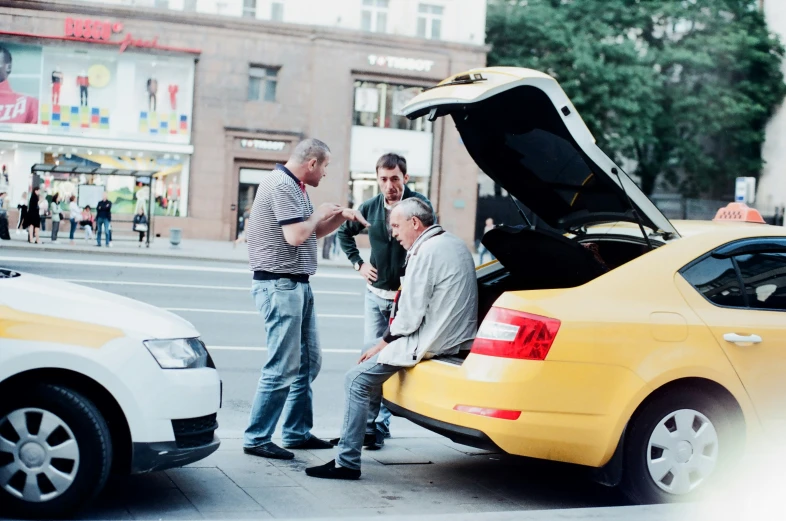 three men look at an open trunk on a street