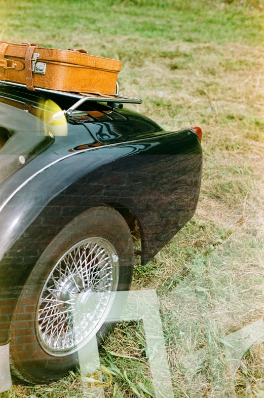 an old fashioned car with luggage on top sitting in a field