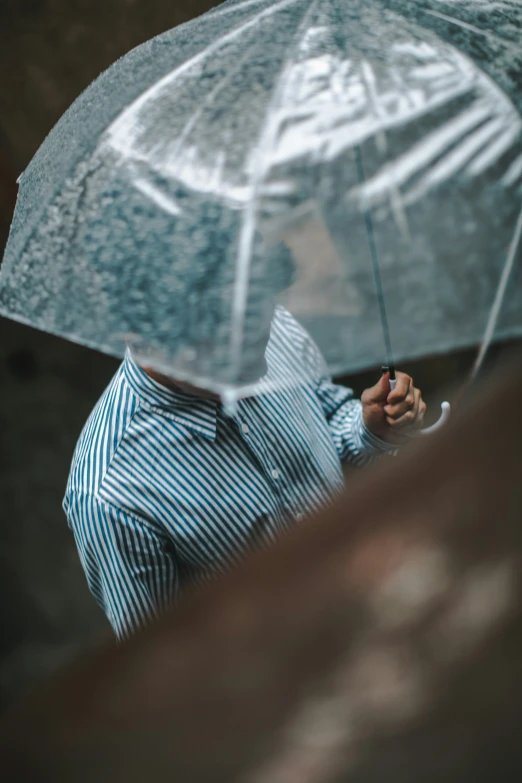 man in a striped shirt holds an umbrella that covers him with an image