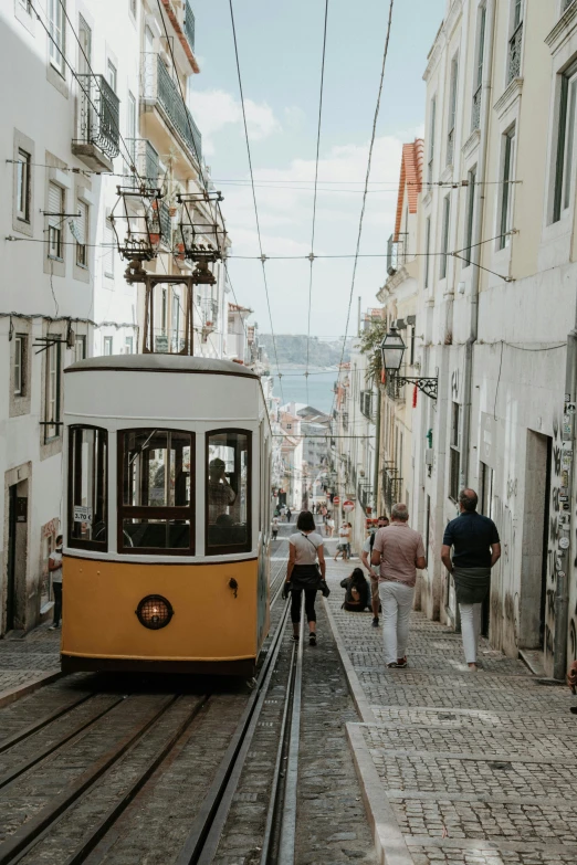 a yellow and white trolley moving down a narrow street