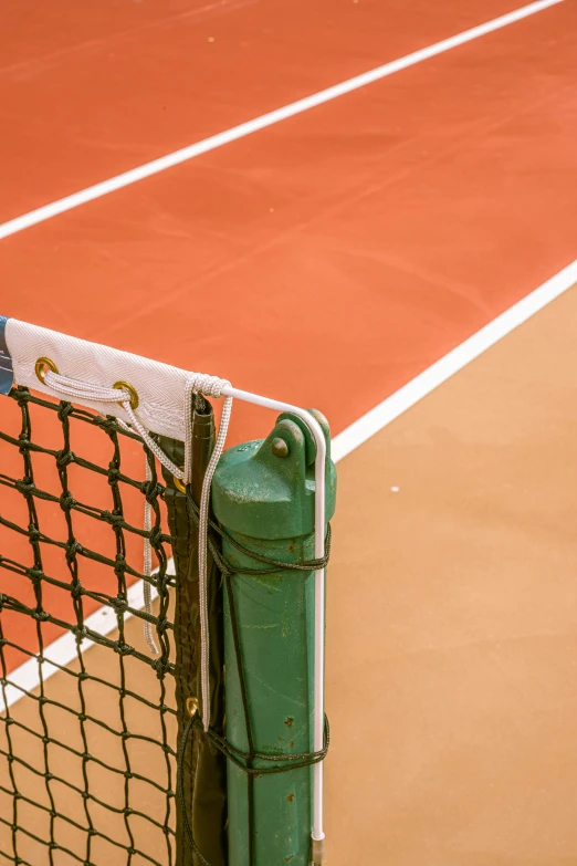 closeup of tennis net with handle on top of clay court