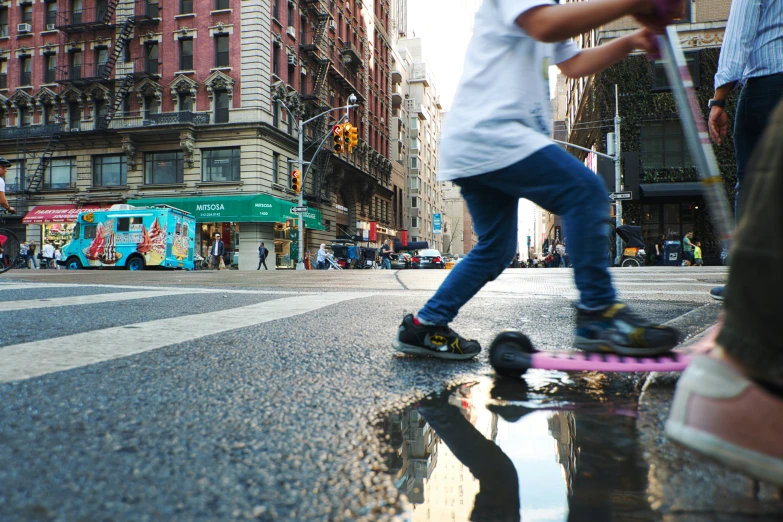 a boy in white shirt riding a skateboard across the street