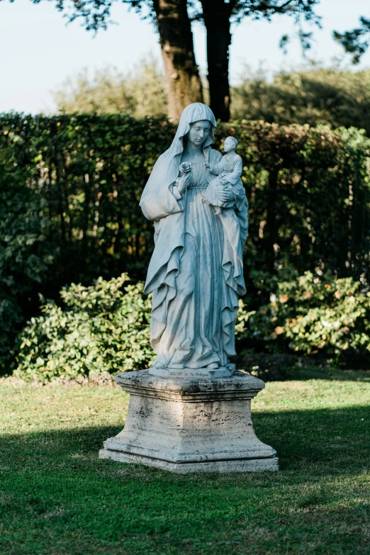 a statue of a woman holding a child near bushes