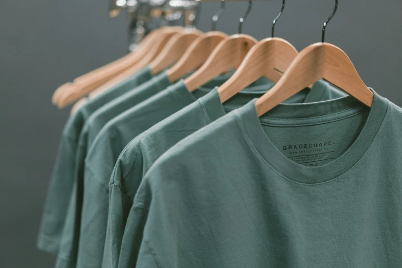 t shirts hanging on wooden hangers in front of a wall