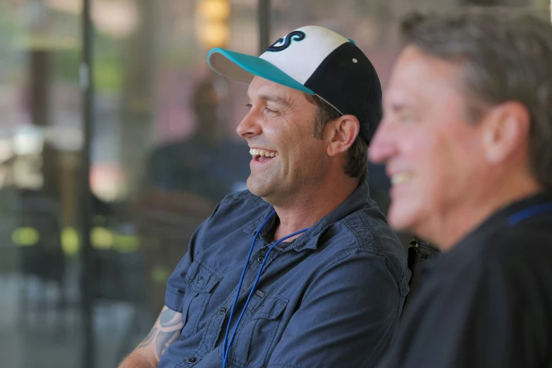 two men are sitting in a window and one is wearing a hat