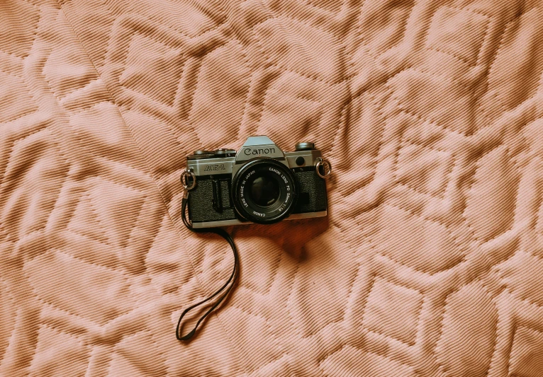 a camera laying on top of a peach colored bed sheet