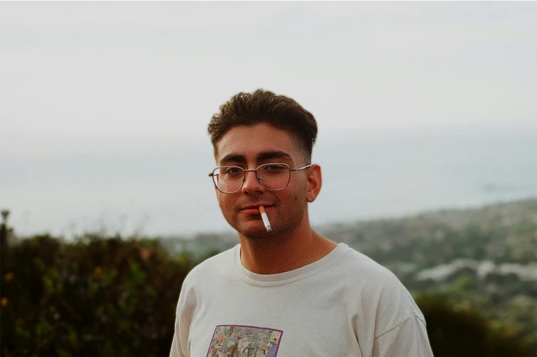 a man standing by bushes and wearing glasses