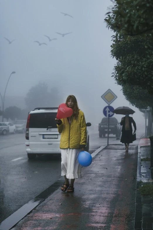 a woman wearing a yellow jacket is walking on a rainy sidewalk
