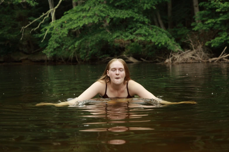 a woman in a swimming suit laying on a board in a lake