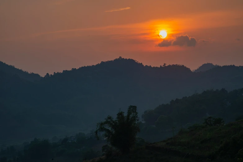 the sun rises over the distant forest on a hill