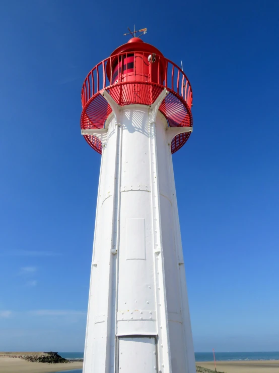 there is a white and red light house next to a beach