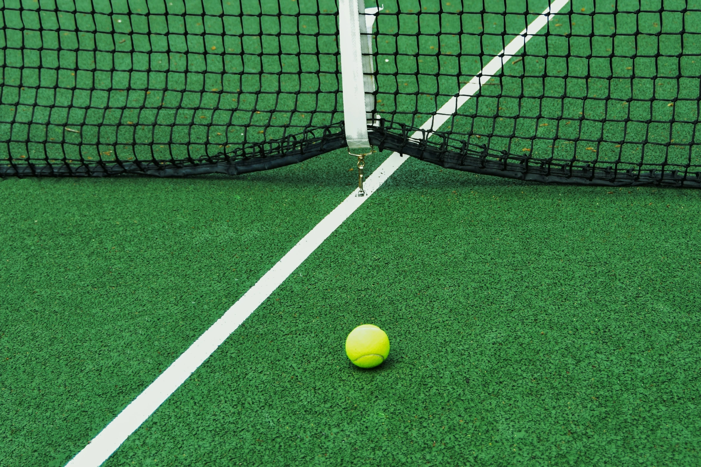 a green tennis court with a black net and yellow ball