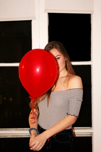 a young woman holding a red balloon up to her face