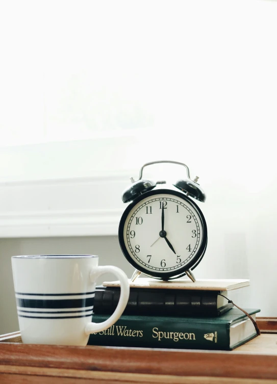 a coffee cup and alarm clock sitting on top of a books