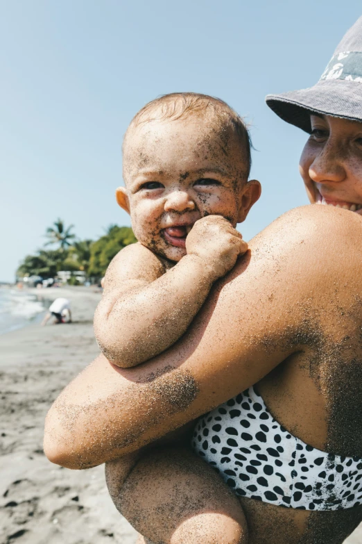 a man holding onto a baby who's crying on the beach