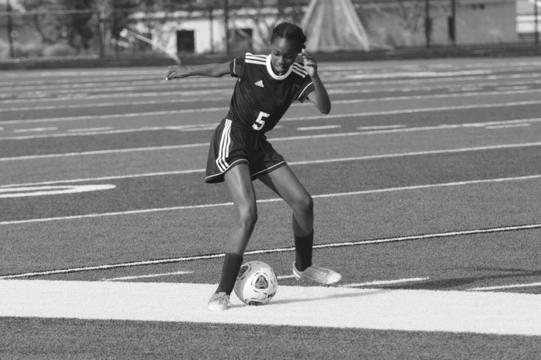 the young woman in a uniform is kicking a soccer ball