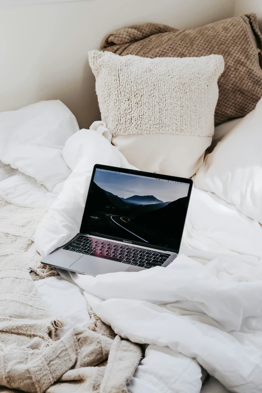 a white bed covered in blankets and a laptop on top of it