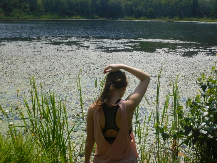 the girl is sitting on a rock near a large pond