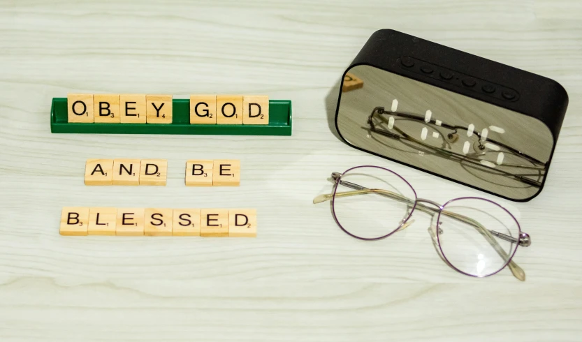 an eyeglass case sits beside a pair of glasses that have words on them and a ruler reading obey god and be blessed