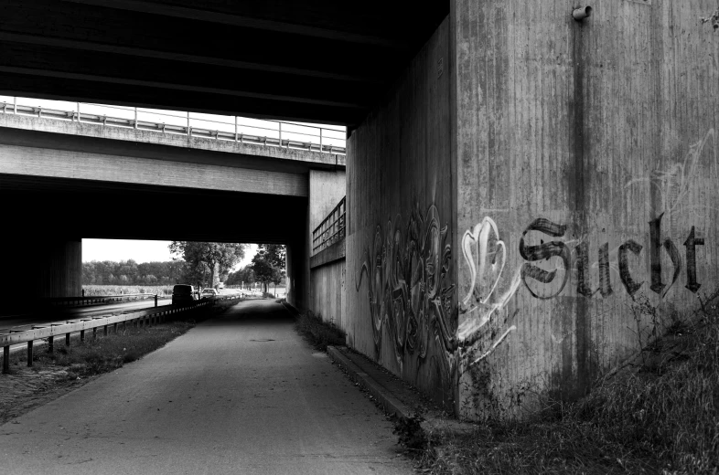 graffiti written on a concrete wall and underneath a train bridge