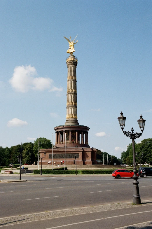 a statue with gold in the top, surrounded by trees and cars