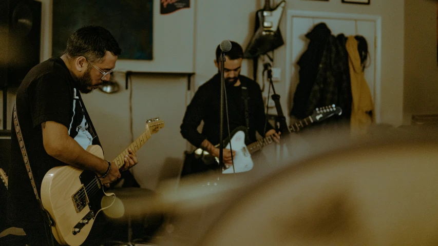 two men playing guitars while sitting in a room