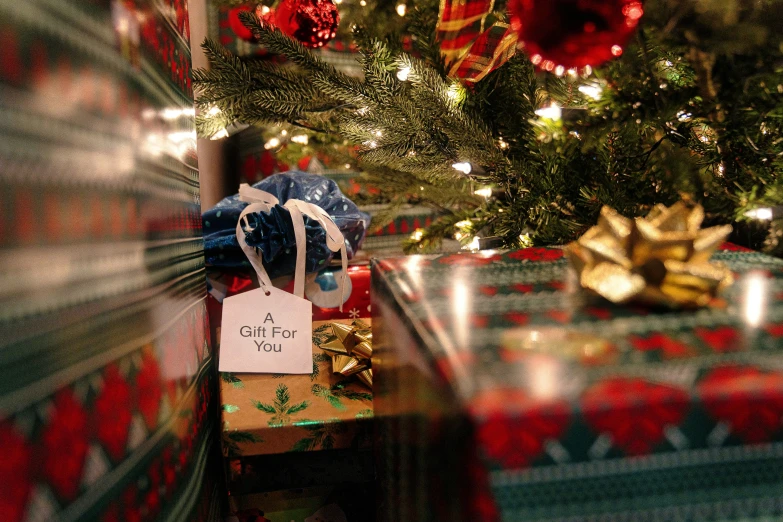 a holiday present wrapped in ribbon sits under a christmas tree with wrapped presents underneath it