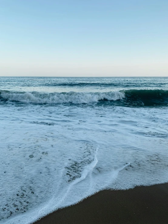 a beach area with waves and one person walking on the sand