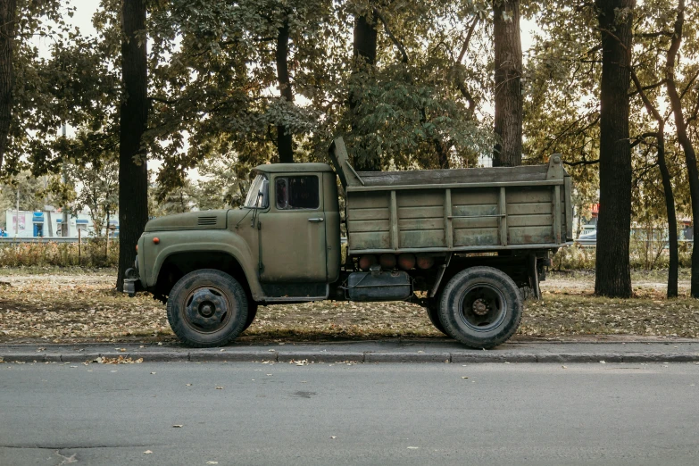 an older military green dump truck parked on a tree lined street