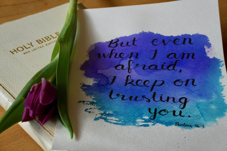 a purple and blue watercolored calligraphy with a flower on a paper