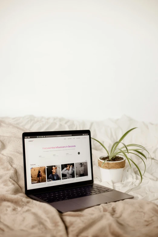 a lap top sits on a bed next to a plant