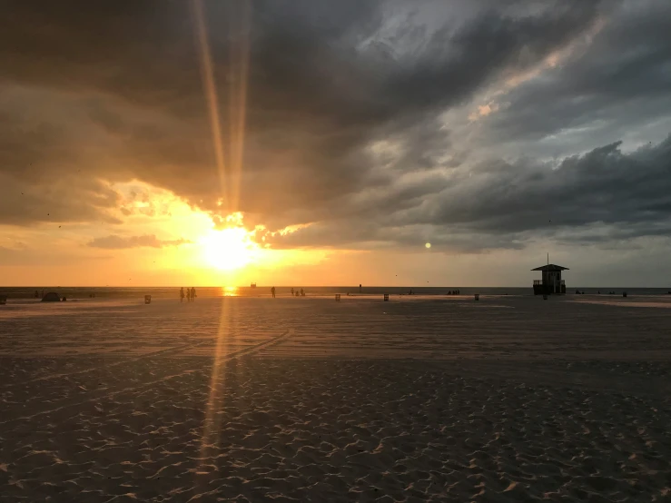 the sun is setting on a cloudy day at the beach