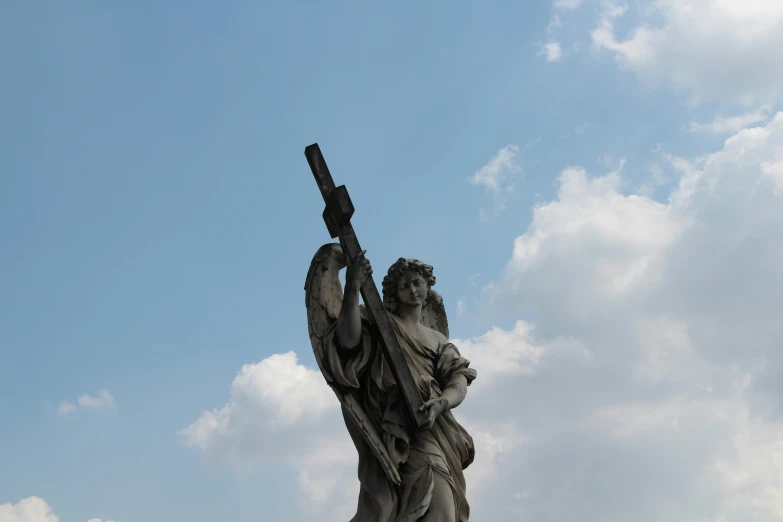 the statue is holding a cross with sky in background