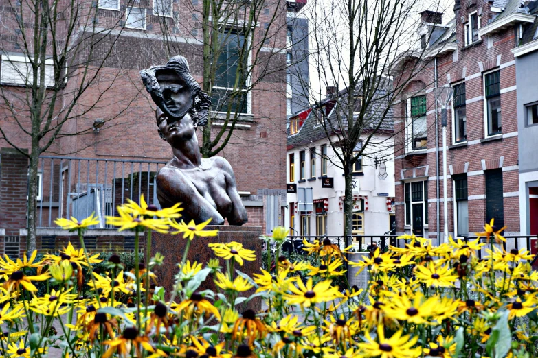 a statue with sunflowers around it on the edge of a road