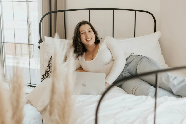 a woman smiling as she uses her laptop on her bed