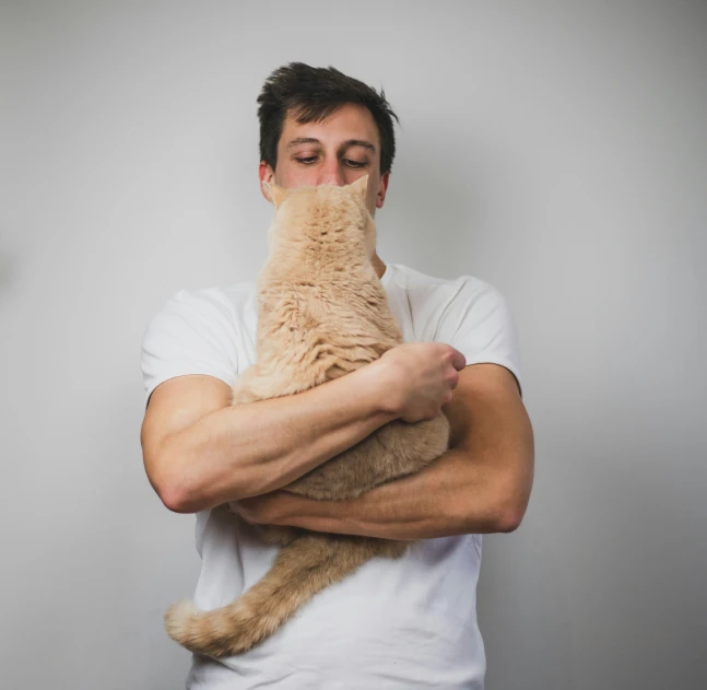 man with cat on chest against white wall