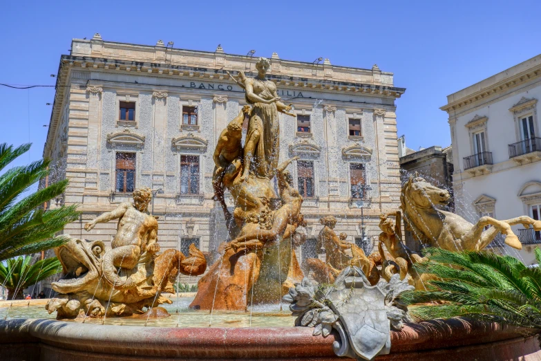 some statues are in the water fountain near a building