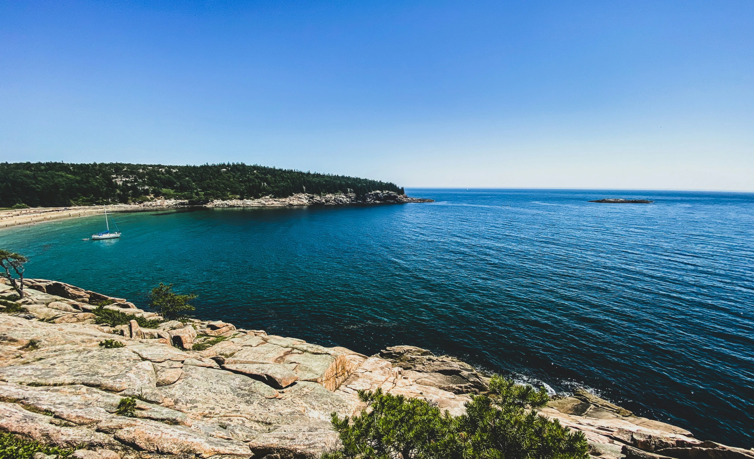 the beach is lined with large rocks under a blue sky