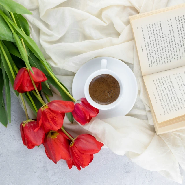 the bouquet of tulips has an open book and cup of coffee