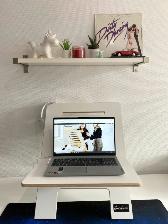 a laptop on a white stand in front of a wall with shelves