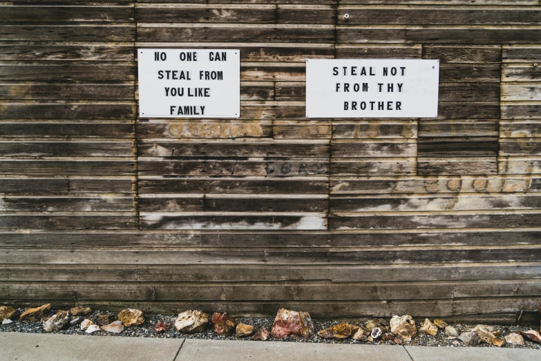 two signs on wooden board set up on the side of a building