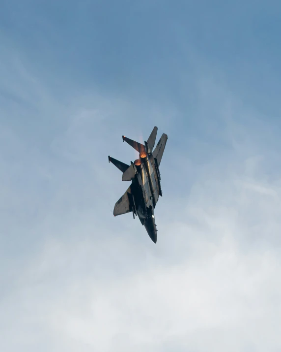 a fighter jet flying through a blue cloudy sky