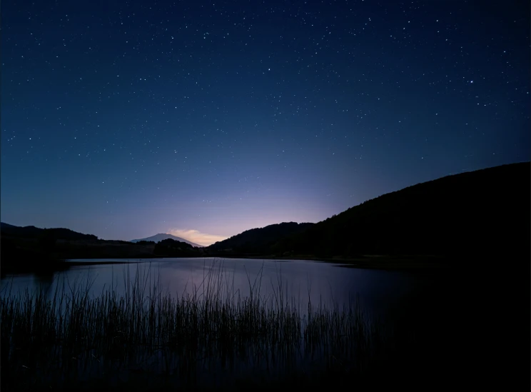 a dark sky with stars above water and mountains