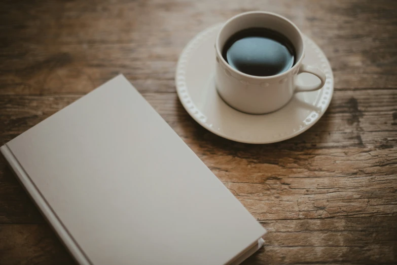 a close up of a cup of coffee next to an open book on a table