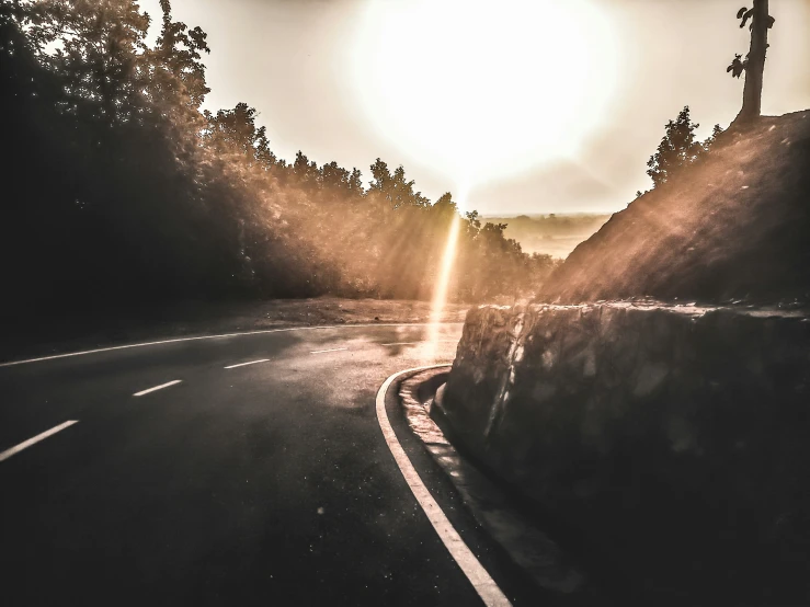 the sun shines through the trees of an empty road