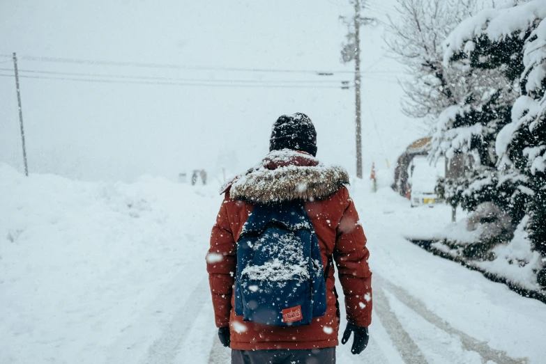 a woman walking down a snow covered road with a blue backpack